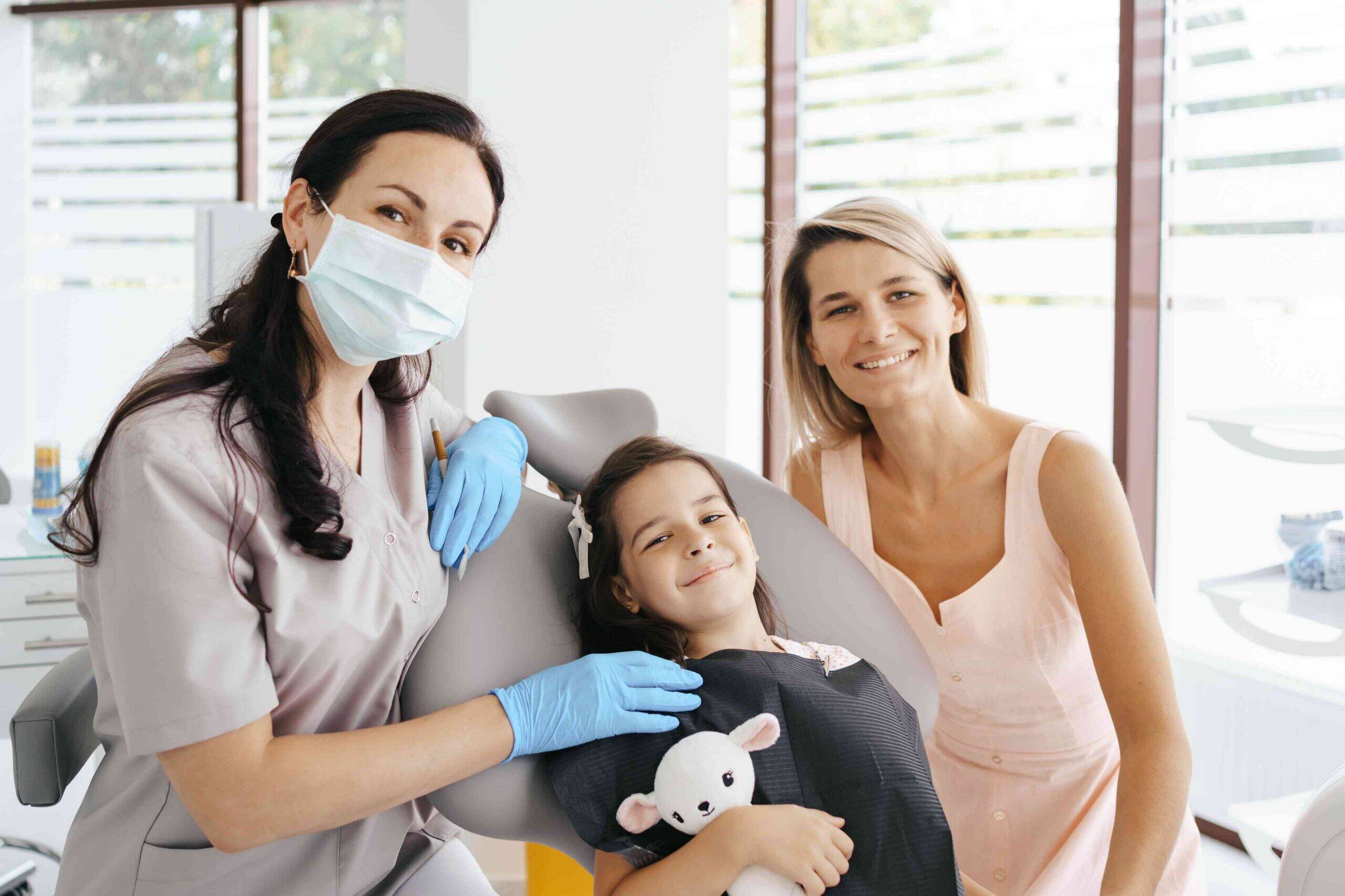 Smiling child patient with dentist and parent in a dental office.